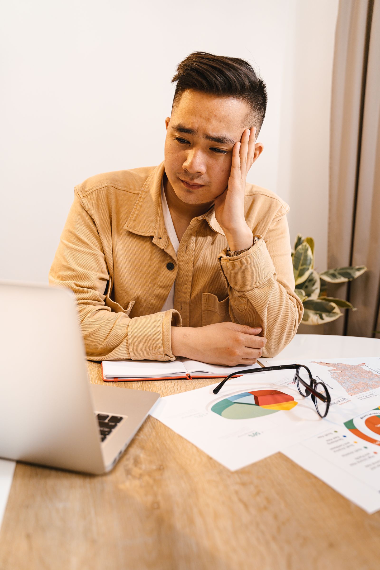 Frustrated person at a laptop surrounded by paperwork